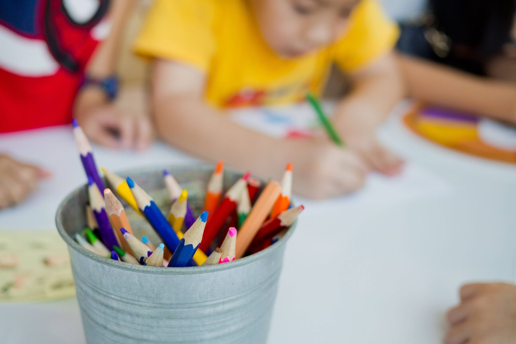 colored pencils in a cup, children coloring in the background